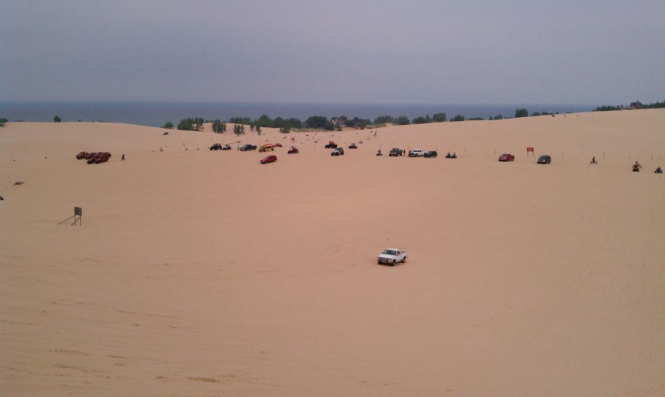 White pickup truck driving on sand dunes with the ocean in the background