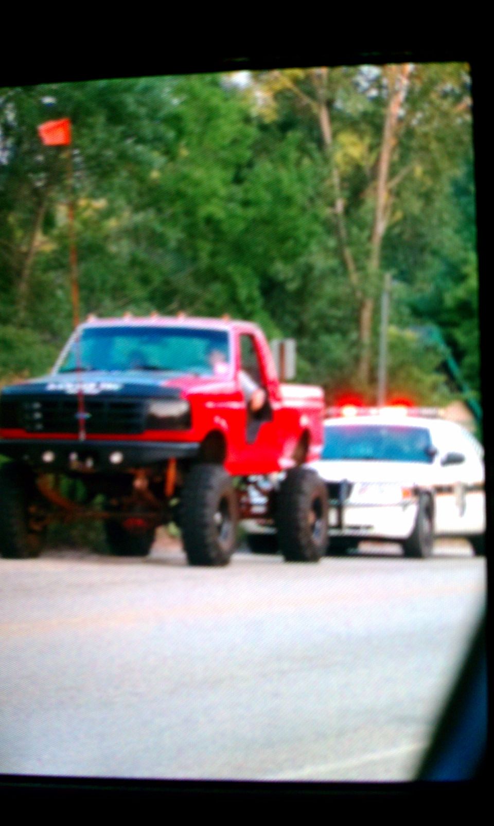 Lifted red pickup truck with big tires next to a white sedan