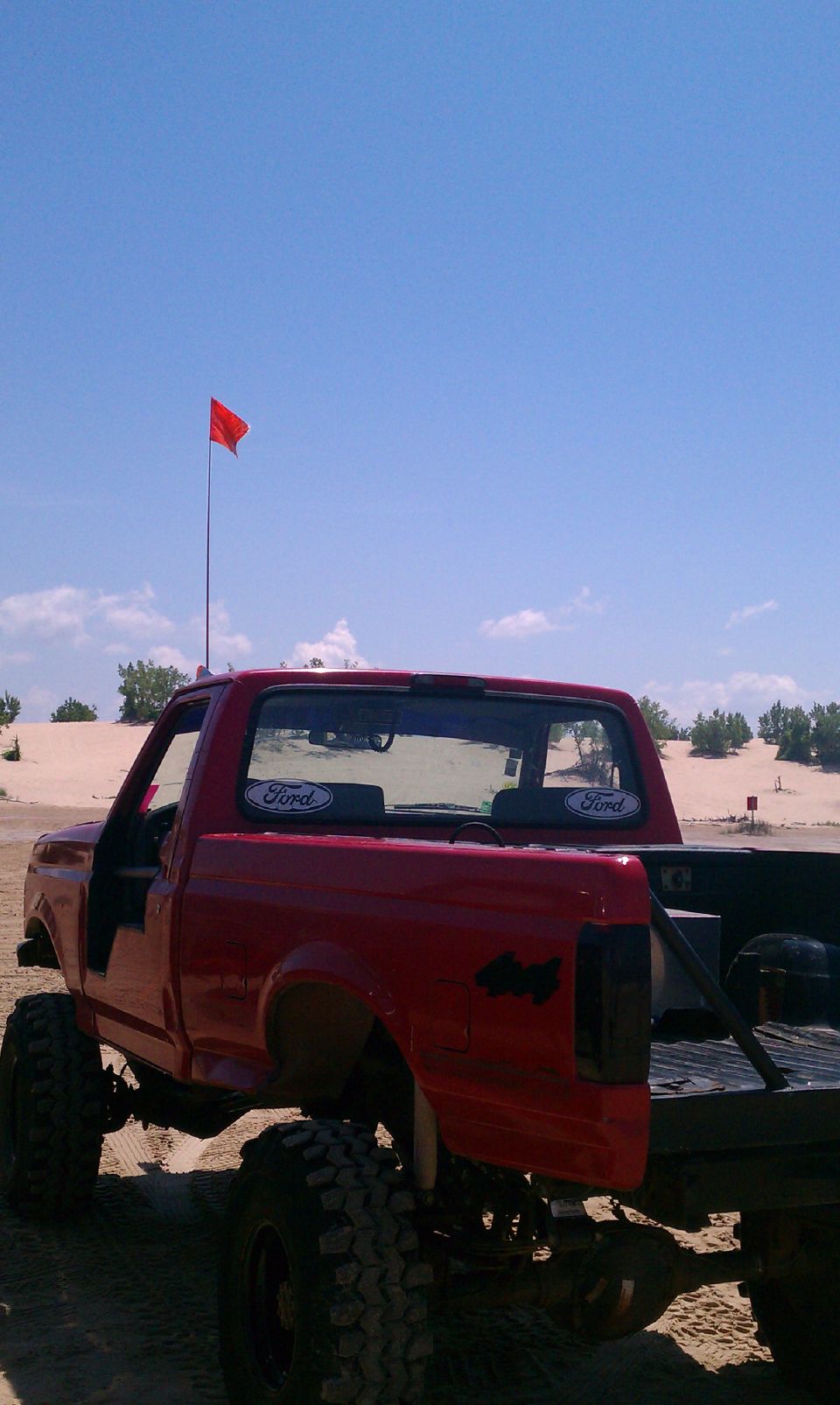 Red 1994 Ford F-250 with Ford decals on rear window, lifted with large tires, on sand dunes