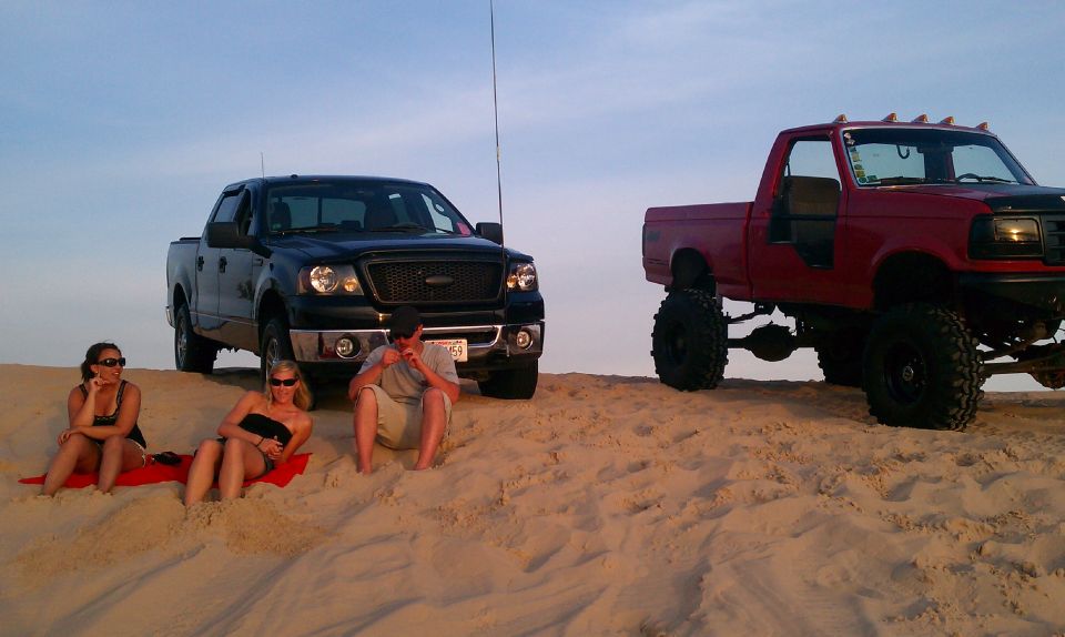 Black pickup truck with people on sand dunes. License plate visible