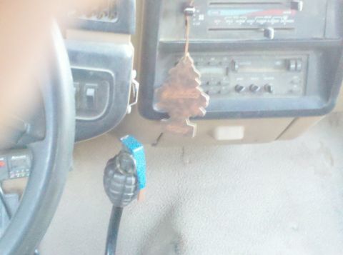 1989 Ford Bronco - The interior of a vehicle features a pine tree air freshener and a grenade-shaped gear shift knob.