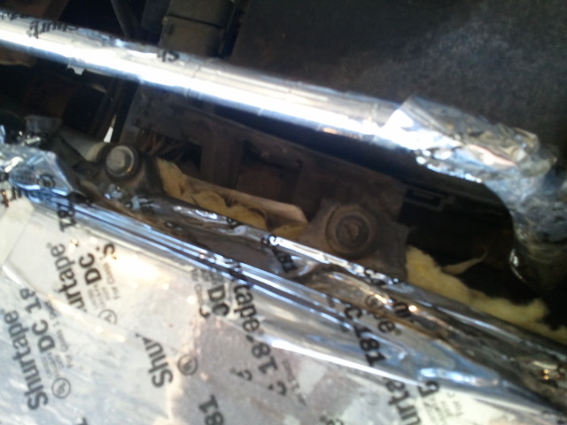 Exposed rusty metal frame and bolts with yellow insulation, surrounded by Shurtape DC 181 foil insulation