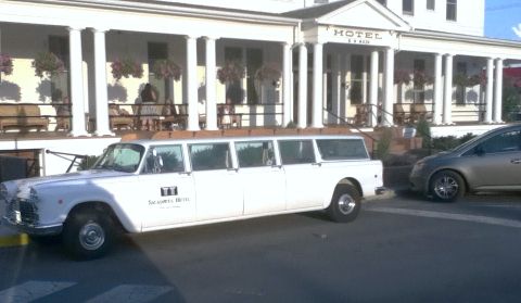 2006 Ford E350 - A white limousine is parked in front of a hotel with a gray car next to it.