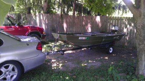 1989 Ford Bronco - A green jon boat on a trailer is parked next to a silver sedan and a red truck.