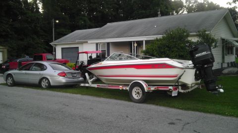 1989 Ford Bronco - A boat on a trailer is parked in front of a house, with a silver sedan and a red pickup truck nearby.