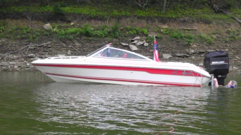 1989 Ford Bronco - A boat with a Mercury outboard motor is partially submerged near a rocky shore, with a person in the water.