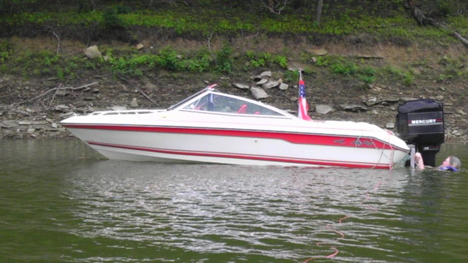 White and red boat with Mercury outboard motor, person in water near stern