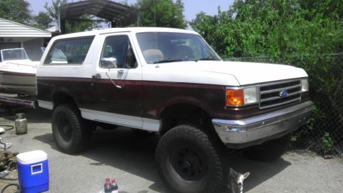 1989 Ford Bronco - A two-tone Ford Bronco is parked in a driveway next to a boat on a trailer.