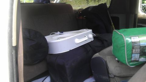 1989 Ford Bronco - The interior of a vehicle is filled with various items, including seats, a portable fan, and a green cargo bag.