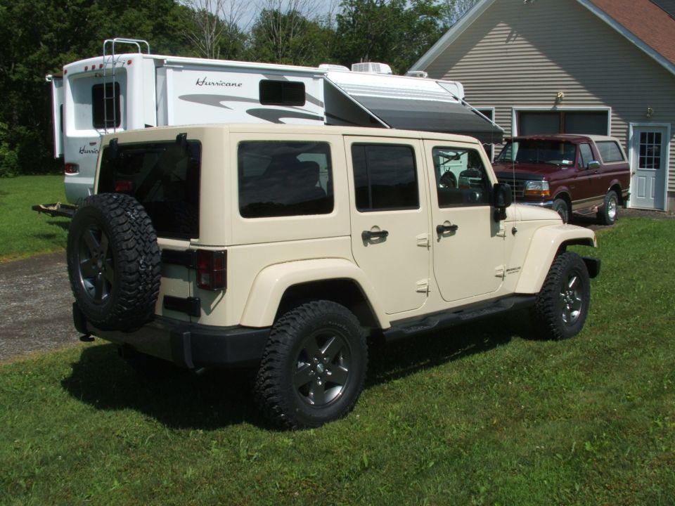 Tan Jeep Wrangler parked on grass, rear spare tire visible