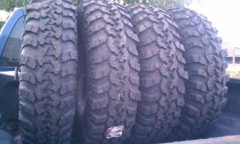 1990 Ford Bronco - Four aggressive off-road tires are loaded into the bed of a truck.