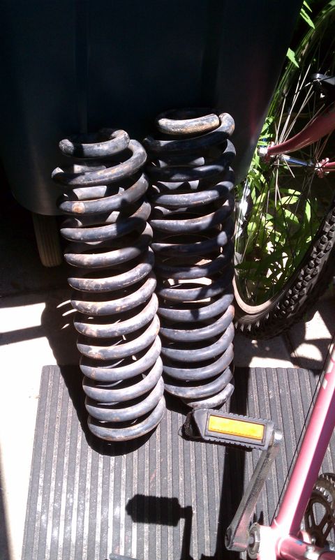 1990 Ford Bronco - Two large metal coil springs and bicycle pedals are visible on a ribbed surface, with a bicycle wheel in the background.