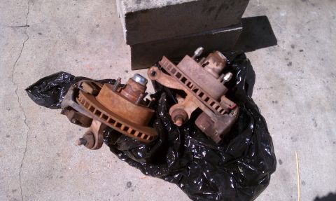 1990 Ford Bronco - Two rusty brake assemblies, likely for a truck or SUV, lie on a concrete surface.