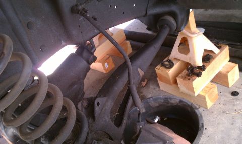 1990 Ford Bronco - The vehicle's front suspension is raised and supported by jack stands and wooden blocks, with a coil spring in view.