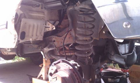 1990 Ford Bronco - Close-up view of the front suspension and frame of a vehicle undergoing maintenance, with components visible on jack stands.