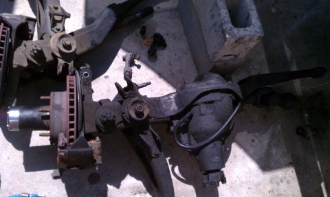 1990 Ford Bronco - Disassembled front axle and suspension components are laid out on a concrete surface.
