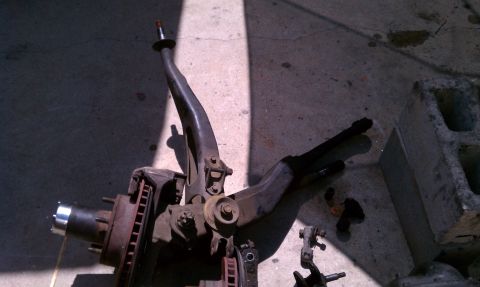 1990 Ford Bronco - Disassembled suspension parts, including a brake rotor and hub, lie on a concrete surface.