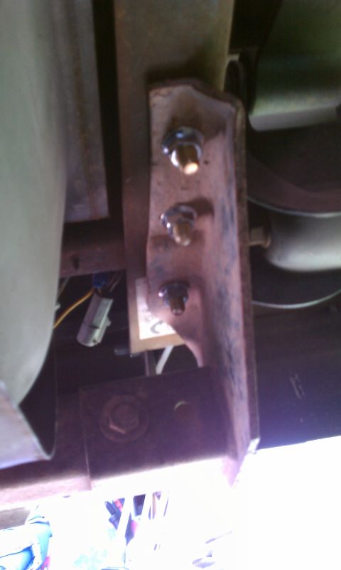 1990 Ford Bronco - Close-up view of a rusted metal bracket with bolts and a wiring harness connector underneath a vehicle.