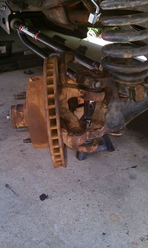 1990 Ford Bronco - Close-up of a heavily rusted front suspension component and brake rotor, with a website URL visible at the bottom.