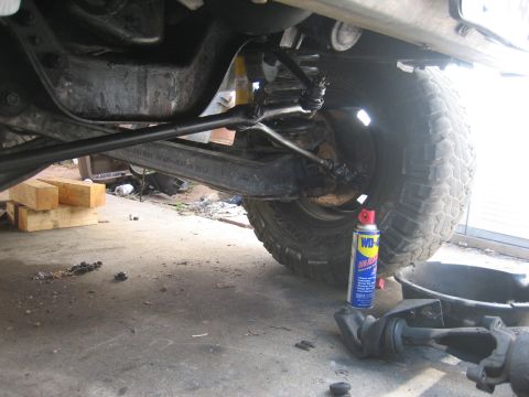 1990 Ford Bronco - Undercarriage view shows suspension parts and a tire, with a can of lubricant and a drain pan on the garage floor.