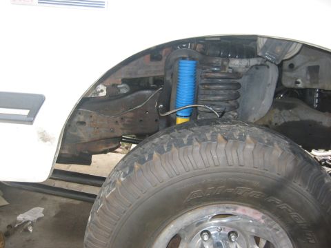 1990 Ford Bronco - Close-up view of the front wheel well, revealing a blue shock absorber and suspension components.