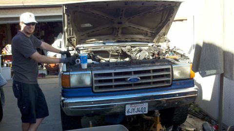 1990 Ford Bronco - A man works on the engine of a blue Ford F-Series truck, which appears to be from the late 1980s.