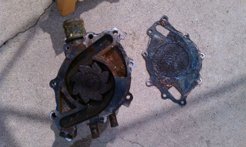 1990 Ford Bronco - A corroded car water pump and its gasket lie disassembled on a concrete surface.