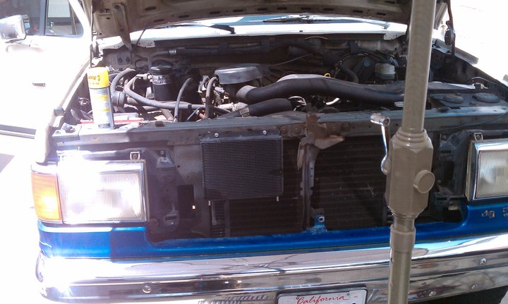 Truck engine bay with hood open, showing engine components and radiator. A yellow spray can sits on the engine