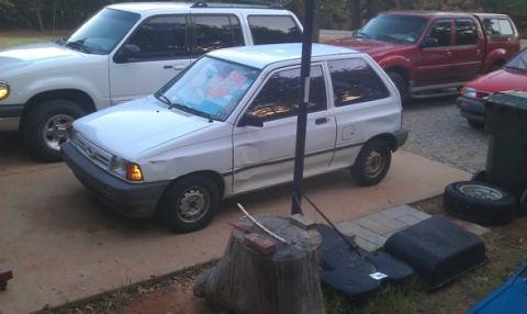 1991 Ford Festiva - A white 1991 Ford Festiva is parked in a driveway with other vehicles.