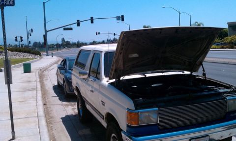 1990 Ford Bronco - This 1990 Ford Bronco is parked on the side of the road with its hood up, revealing the engine.