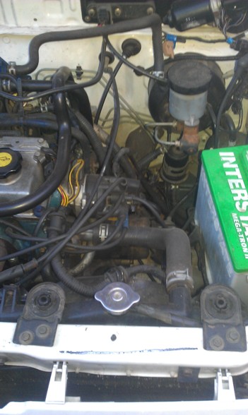 1991 Ford Festiva - The engine bay of a vehicle is shown, various hoses and a green battery.