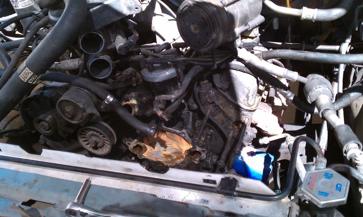 engine bay with hoses, belts, and pulleys visible. Some parts appear corroded