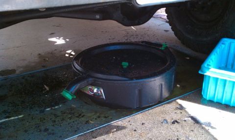 1990 Ford Bronco - Draining oil from a vehicle into a pan on a concrete surface.