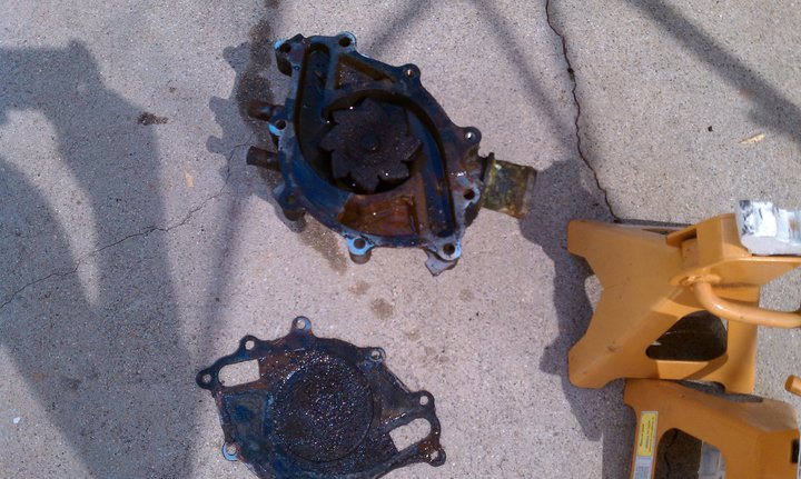 Used car water pump and gasket on concrete next to a yellow jack stand