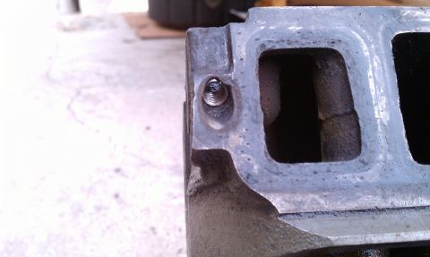 1990 Ford Bronco - A close-up view of a metal engine intake manifold part, showing a bolt inserted into one of its ports.