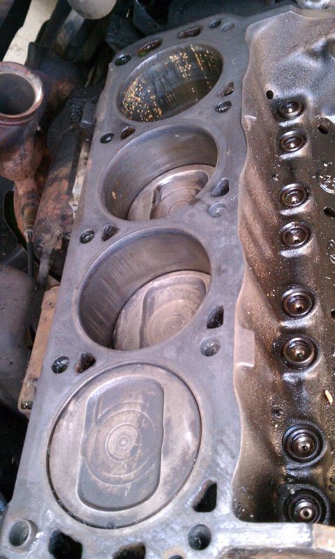 1990 Ford Bronco - Close-up view of an engine's cylinder head, revealing the pistons within the cylinders and signs of wear.
