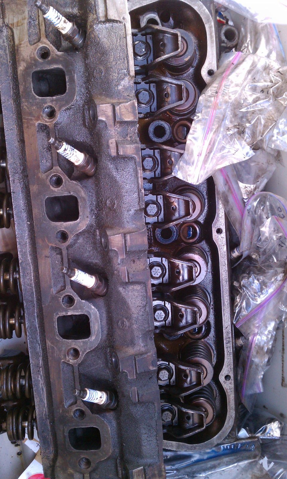 Engine cylinder head with spark plugs and rocker arms visible. Some parts are in plastic bags
