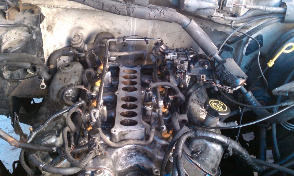 Engine bay with intake manifold removed, showing fuel injectors and engine block. Some grime and dirt are visible