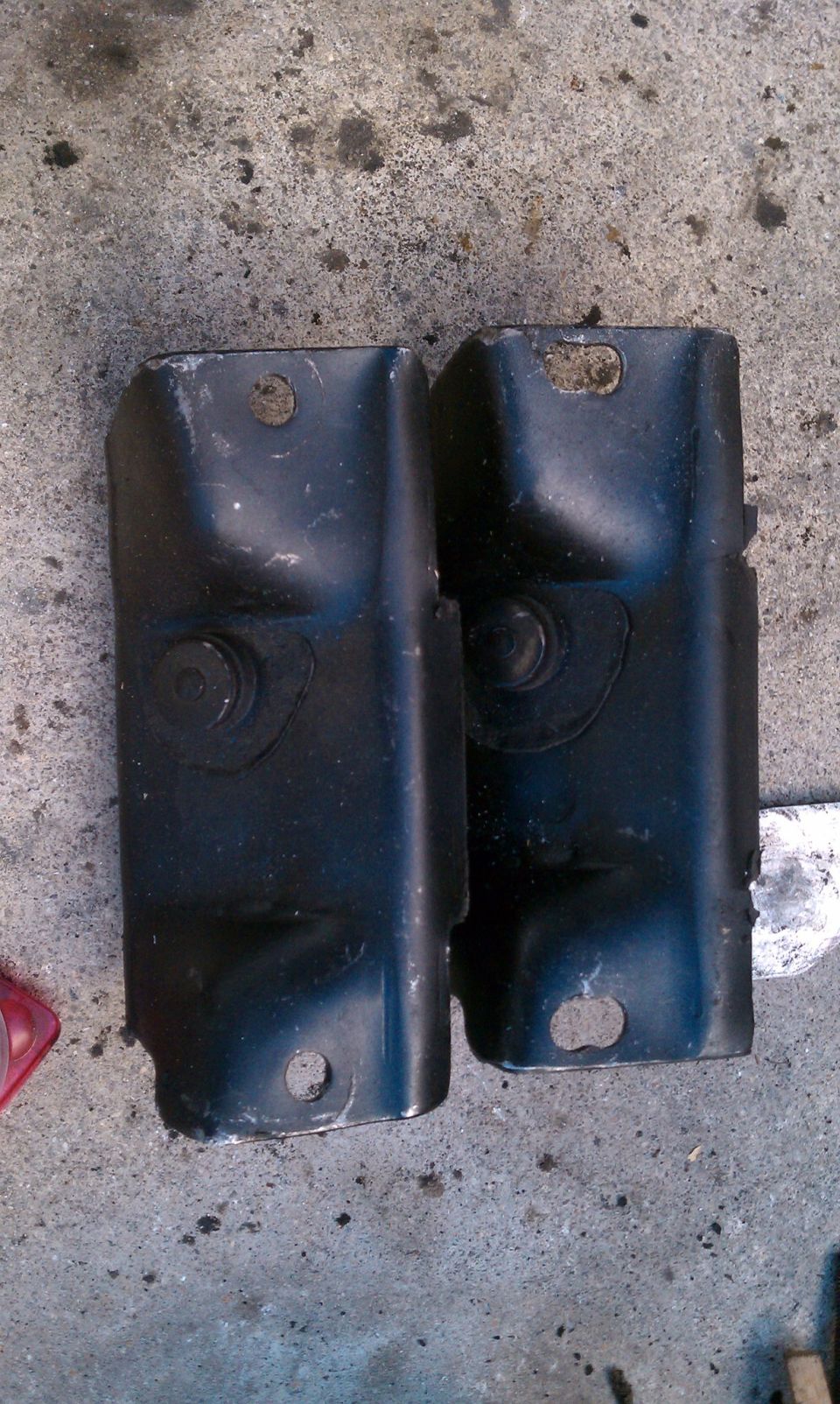 Two black metal brackets with bolt holes on a concrete surface