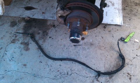 1990 Ford Bronco - Close-up of a vehicle's brake assembly, showing the rotor, hub, and brake line on a concrete surface.