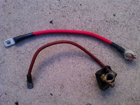 1990 Ford Bronco - Two automotive battery cables, one red and one dark red, lie on a concrete surface.