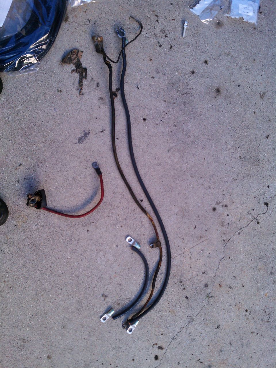 Battery cables and wiring harness laid out on concrete. One red cable with a terminal, two black cables with terminals