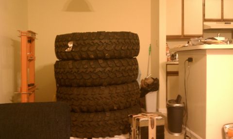 1990 Ford Bronco - Several large off-road tires are stacked indoors next to a kitchen counter.