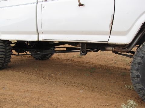 1995 Ford Bronco - Close-up view of the rear suspension system on a white truck, large off-road tires and custom linkage components.