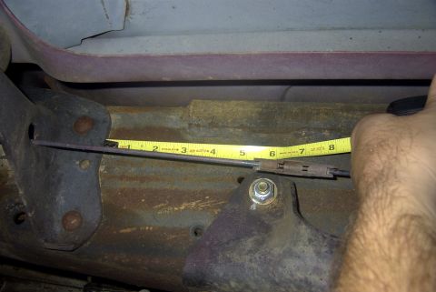 1994 Ford Bronco - A tape measure is used to measure a cable assembly on the underside of a vehicle, with visible rust and structural components.