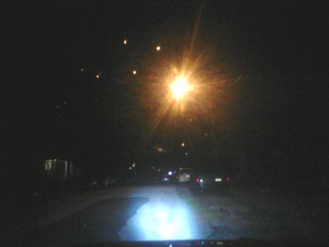 1988 Ford Bronco - A dark street at night is illuminated by a bright light, with several vehicles visible in the distance.