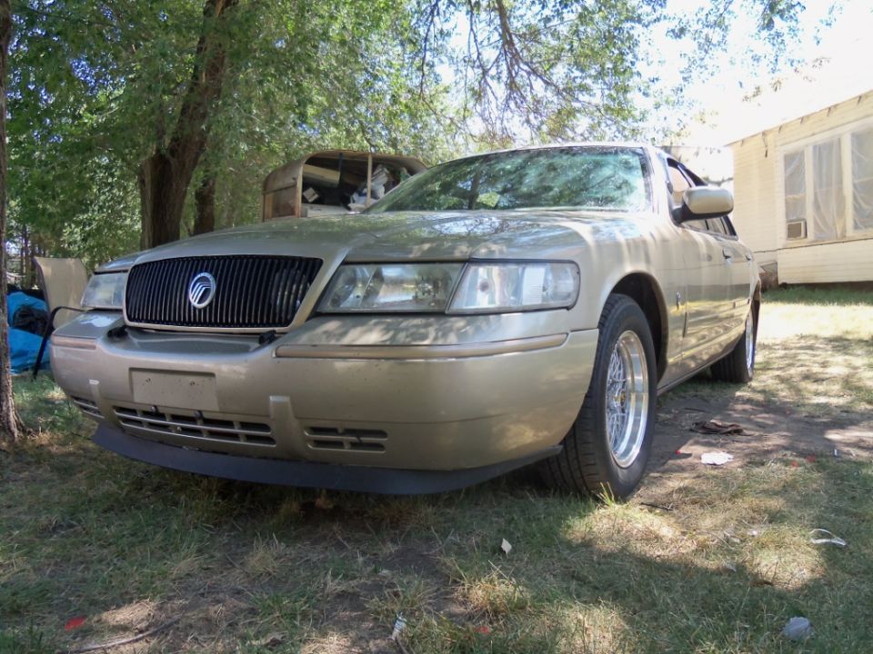 Gold 2000 Mercury Grand Marquis with a black grille and aftermarket wheels parked on grass