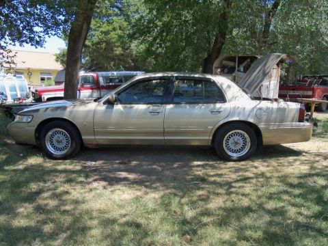 2000 Mercury Grand Marquis - Gold sedan parked outdoors with its trunk open, showing some damage to the door trim.