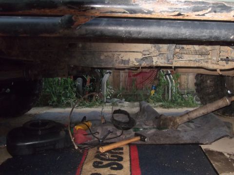 1989 Ford Bronco - Tools and parts are laid out on the ground beneath a vehicle's rusty undercarriage.
