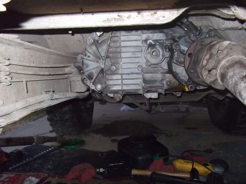 1989 Ford Bronco - Underside view of a vehicle's transmission and driveshaft, with tools and fluids visible on the ground.